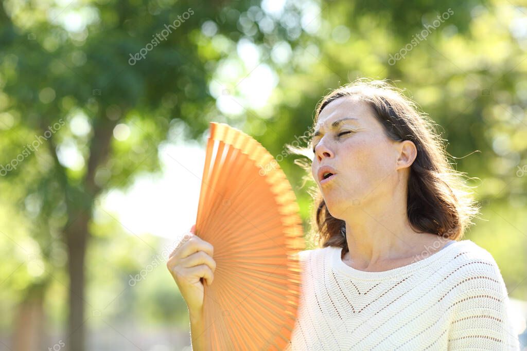Adult woman using fan refreshing suffering heat stroke standing in the park at summer