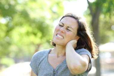 Adult woman in pain suffering neck achestanding in the park at summer clipart