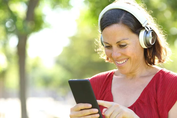 幸せな大人の女性は公園でヘッドフォンでスマートフォンで音楽を聞いて — ストック写真