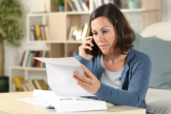 Serious adult woman checking letter calling on smart phone sitting in the livingroom at home