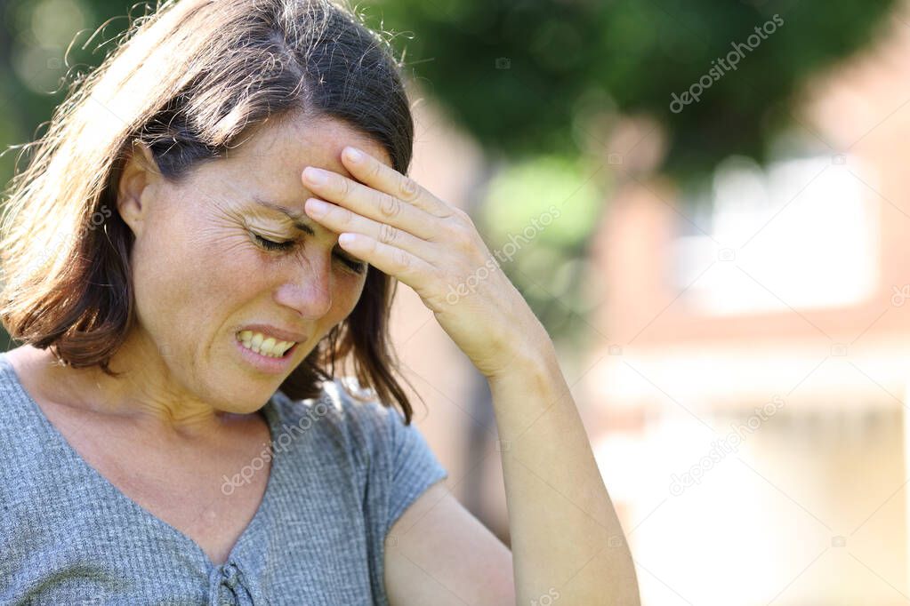 Adult woman in pain suffering headache standing in a park in summer