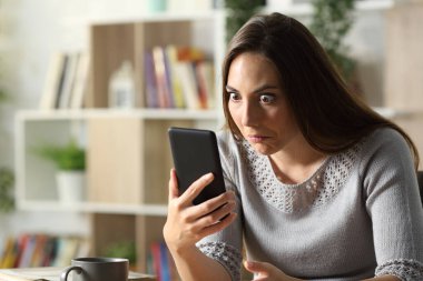 Kafası karışmış bir kadın, evdeki masada oturan akıllı telefona şaşırmış bakıyor.