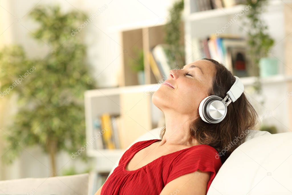 Relaxed adult woman listens to music with headphones in the coach at home
