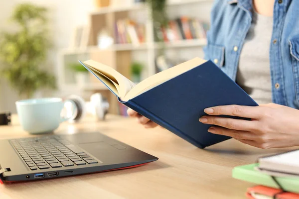 Close up of a student woman hand reading a hardcover book sitting a desk at home