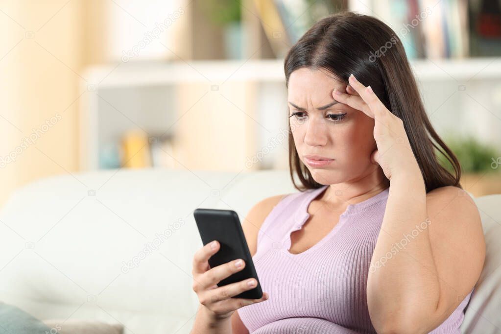 Frustrated woman checking smart phone finding mistake sitting on a couch at home