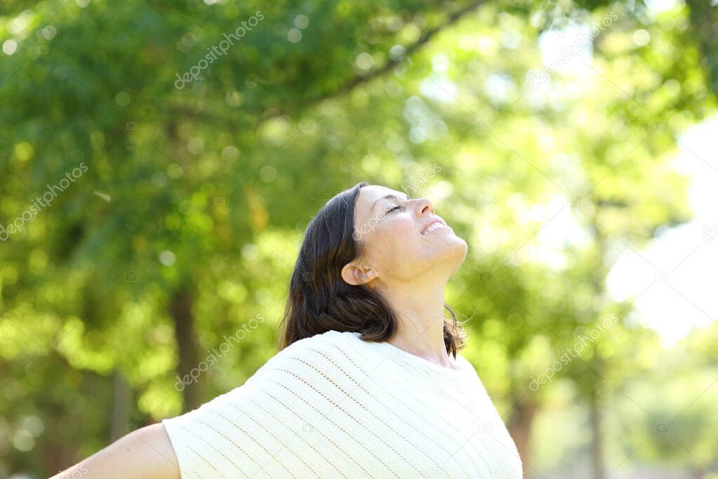 Middle aged woman breaths fresh air standing in a park a sunny day of summer