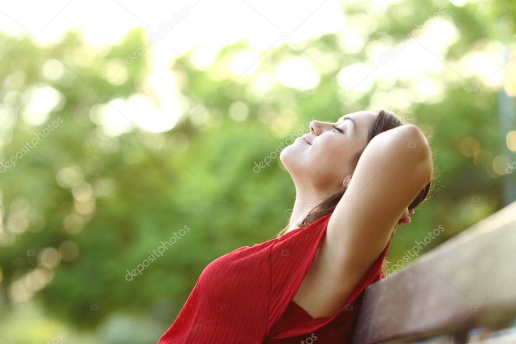 Side view portrait of a relaxed woman in a park breathing fresh air sitting on a bench