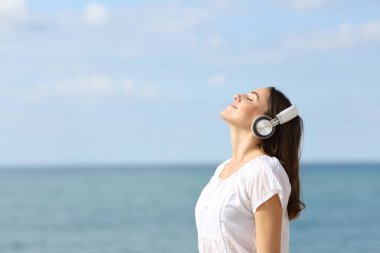 Rahat bir gencin yan görünüm portresi. Temiz hava soluyor. Plajda meditasyon yapan kulaklıklarla müzik dinliyor.