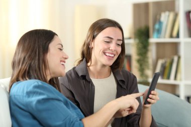 İki mutlu arkadaş telefonda medyayı izlerken gülüyor. Oturma odasındaki kanepede. 