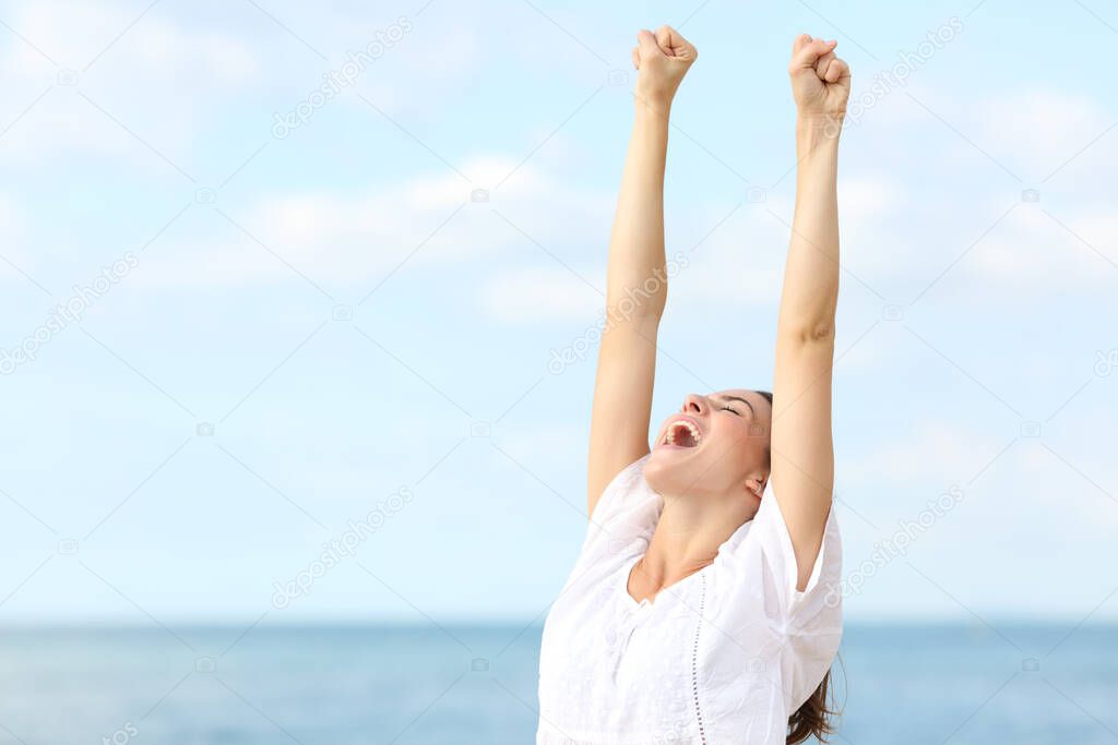 Excited woman celebrating raising arms and screaming on the beach on summer