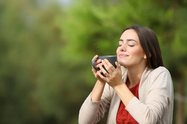 Relaxed woman holding coffee cup breathing fresh air sitting in a park