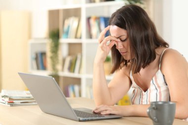 Evdeki masada dizüstü bilgisayarla göz yorgunluğu çeken bir kadın.