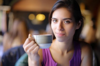 Kahve fincanı tutan memnun restoran müşterisi sana bakıyor.