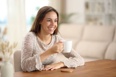 Elinde kahve fincanı olan mutlu bir kadın evdeki oturma odasına bakıyor.