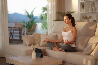 Yogi gün batımında yoga yapıyor. Evdeki bir kanepede oturuyor.