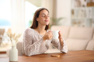 Evdeki oturma odasındaki ahşap masada kahve kokusu alan bir kadın.