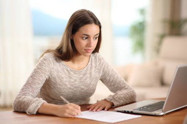 Evdeki dizüstü bilgisayarda içeriği kontrol eden kağıt imzalayan kadın