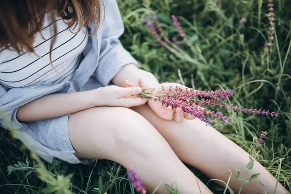 Chica sentada en verde hierba sosteniendo flores — Foto de Stock