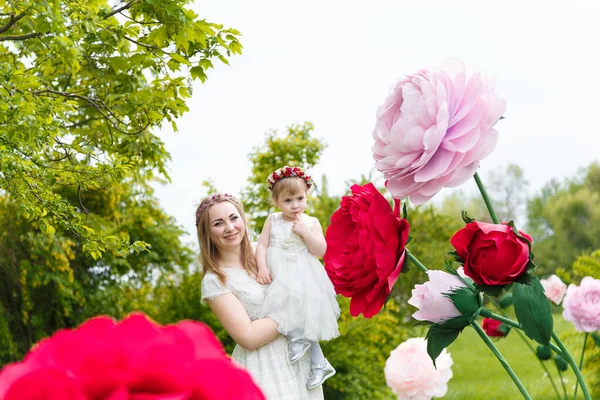 穿着白色衣服的小女孩和母亲在绿茵的草坪上玩耍 背景是高人造玫瑰花 花朵和童年的概念 — 图库照片