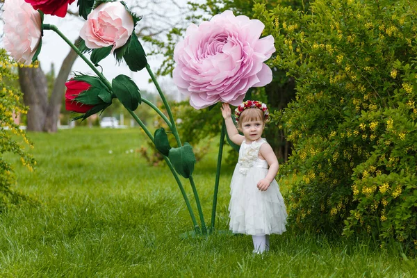 Beyaz Elbiseli Küçük Kız Arka Planda Yüksek Yapay Gül Çiçekleri — Stok fotoğraf