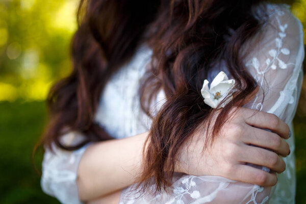 Hands of teenager girl in white dress with flower in her long dark hair in apple garden. Spring blooming and youth concept.