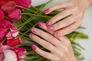 Laleler tırnak tasarımı, bahar çiçekleri arka planında manikürlü tırnaklar. Güzellik konsepti, yakın çekim..