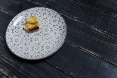 Küçük bir parça ya da bir parça ekmek, siyah ahşap masa zemininde bir tabakta kalmış. Lezzetli ve sağlıksız bir ürün. Diyet, beslenme, yeme alışkanlıkları. Az kilolu ya da fazla kilolu. Boşluğu kopyala.