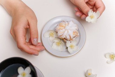 Kadın eli, bir fincan yasemin çayı, beyaz masadaki şeker tozlu pasta..