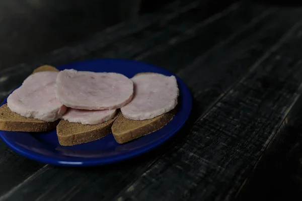 Sandwich Pâine Neagră Felii Cârnați Placă Albastră Picioare Fundal Negru — Fotografie, imagine de stoc