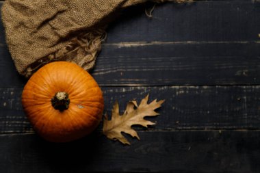 Kuru sonbahar yapraklı balkabağı, otlar ve siyah ahşap arka planda çuval bezi. Sonbahar hasadı, sağlıklı organik gıda konsepti. Boşluğu kopyala.