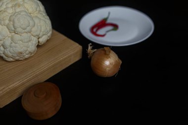 Karnabahar, soğan ve siyah masada kırmızı acı biber. Mutfakta yemek hazırlıyorum. Boşluğu kopyala.