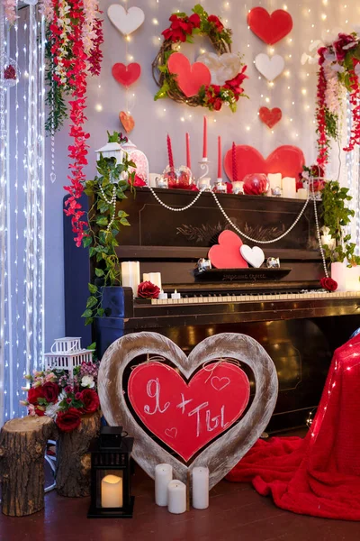 Valentines Day concept. Piano decorated with candles, red wooden hearts and flowers. Chair with red plaid and soft focused inscription Me + You on the foreground.
