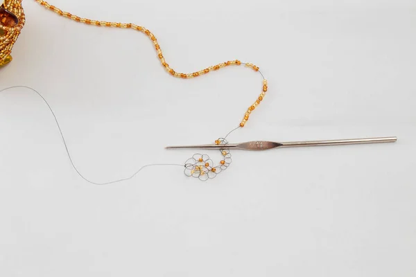 Crochet and black wire with golden or amber colored beads and some loops in process of making handmade jewelry, bijouterie on white fabric background. Workshop, leisure, hobby concept.