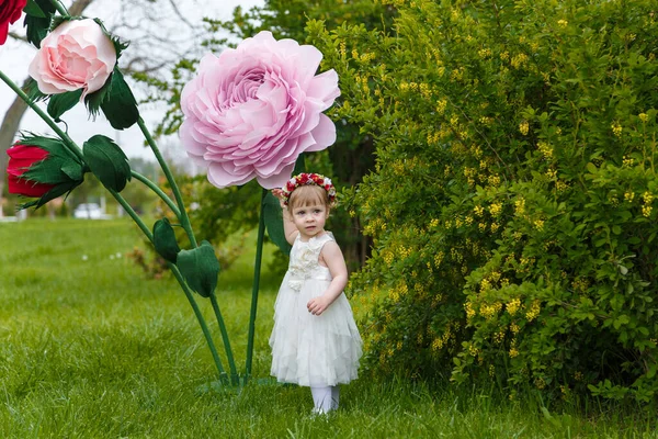 Beyaz Elbiseli Küçük Kız Arka Planda Yüksek Yapay Gül Çiçekleri — Stok fotoğraf
