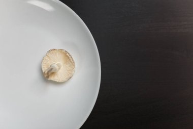 Siyah masada beyaz tabakta çiğ şampiyon mantarı. Yeterli yiyecek ya da aşırı doygunluk konsepti değil. Diyet, beslenme, sağlıklı ve sağlıksız yeme alışkanlıkları, kilolu ya da zayıf konsept.