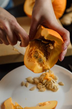 Kadın mutfak tahtasındaki kabaktan tohumları alıyor, sadece elleri görünüyor. Sonbahar mevsimlik sebzeleri. Sağlıklı yeme alışkanlıkları, organik vejetaryen gıda konsepti.