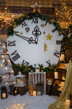 Altın çelenk ışıkları, oyuncak kalpler, koniler, parlak yıldızlar, kar taneleri ve kahverengi ahşap arka planda mumlar olan büyük dekoratif saat. Mutlu Noeller ve yeni yıl gece yarısı konsepti.