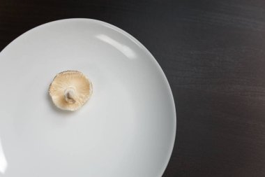 Siyah masada beyaz tabakta çiğ şampiyon mantarı. Yeterli yiyecek ya da aşırı doygunluk konsepti değil. Diyet, beslenme, sağlıklı ve sağlıksız yeme alışkanlıkları, kilolu ya da zayıf konsept.