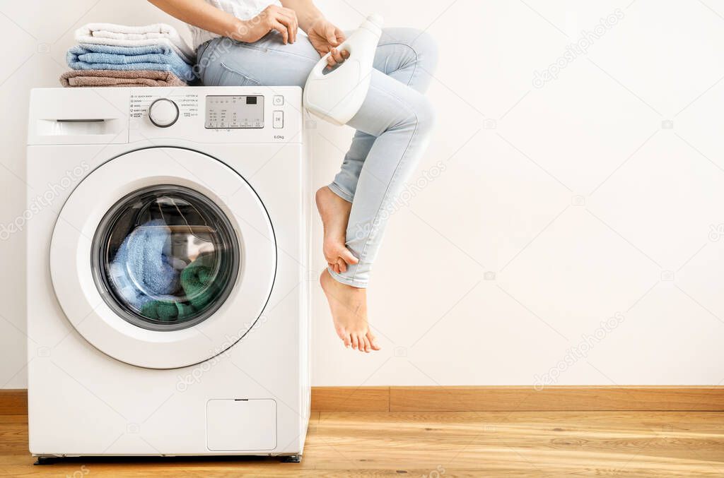 Young woman with washing gel sitting on washing machine