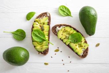 Beyaz ahşap arka planda baharatlı avokado sandviçi. Üst görünüm.