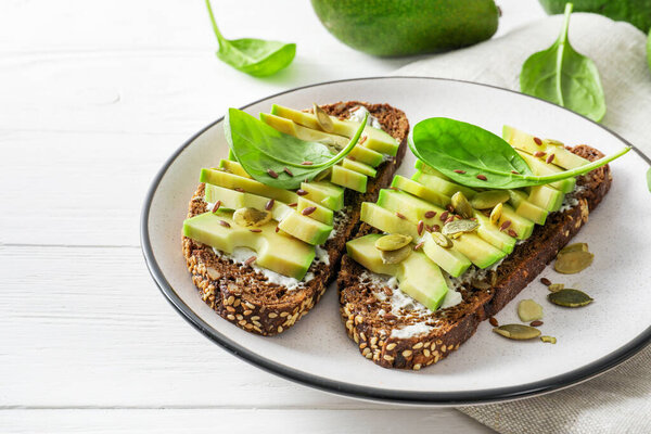 Seasoned avocado sandwiches in plate on white wooden background.