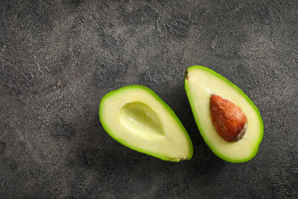 Whole and halved avocado fruits on dark background. Top view.
