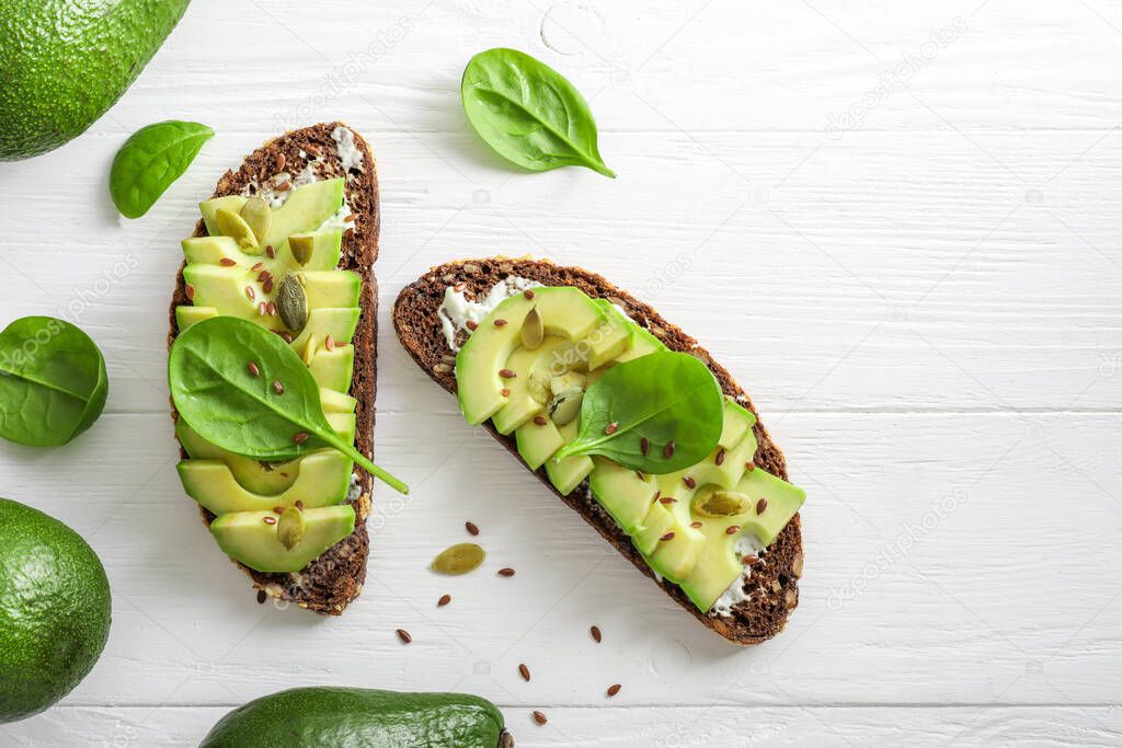 Seasoned avocado sandwiches on white wooden background. Top view.