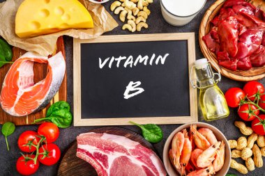 Koyu arkaplandaki yüksek B vitamini kaynakları: süt, karaciğer, zeytinyağı, domates, karides, fıstık, sığır eti, ıspanak, somon, keshew, peynir. Üst görünüm.