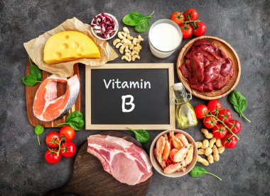 Koyu arkaplandaki yüksek B vitamini kaynakları: süt, karaciğer, zeytinyağı, domates, karides, fıstık, sığır eti, ıspanak, somon, keshew, peynir, haricot. Üst görünüm.