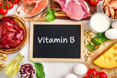 Beyaz zemin üzerindeki yüksek B vitamini kaynakları: süt, karaciğer, zeytinyağı, domates, karides, fıstık, biftek, ıspanak, somon, keshew, peynir, haricot, yumurta. Üst görünüm.