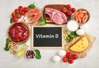 Beyaz zemin üzerindeki yüksek B vitamini kaynakları: süt, karaciğer, zeytinyağı, domates, karides, fıstık, biftek, ıspanak, somon, keshew, peynir, yumurta, haricot. Üst görünüm.