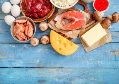 Mavi ahşap arka planda yüksek D vitamini kaynakları: ciğer, karides, somon, peynir, tereyağı, kırmızı havyar, yumurta, mantar, süzme peynir. Üst görünüm.