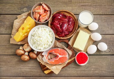 Ahşap zemin üzerindeki yüksek D vitamini kaynakları: süt, karaciğer, karides, somon, peynir, tereyağı, kırmızı havyar, yumurta, mantar, süzme peynir. Üst görünüm.