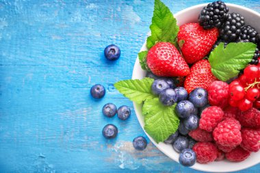 Mavi ahşap arka planda çeşitli yabani böğürtlenlerle seramik kase. Üst Manzara. Boşluğu kopyala.